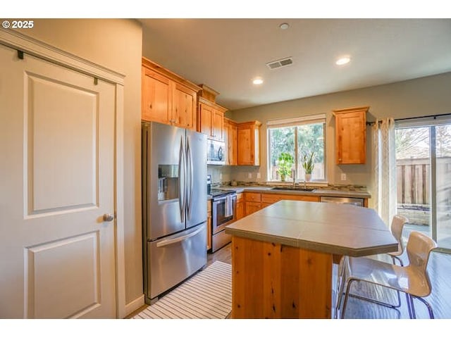 kitchen featuring stainless steel appliances, a sink, visible vents, a wealth of natural light, and a center island