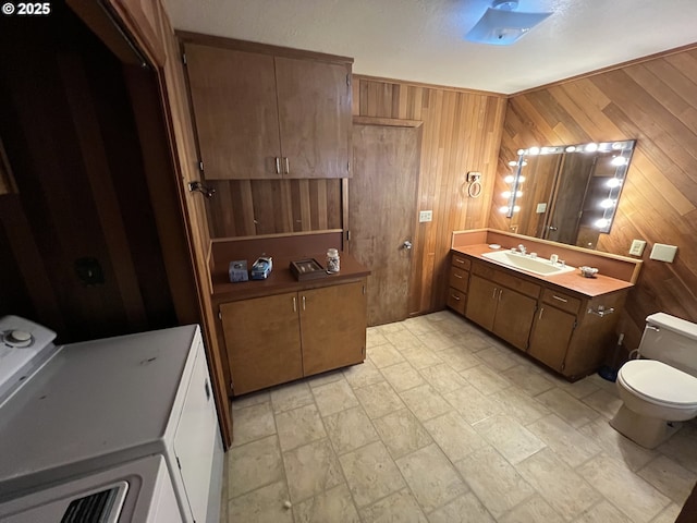 bathroom featuring washing machine and clothes dryer, wooden walls, vanity, and toilet