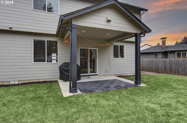 back house at dusk featuring a patio and a yard