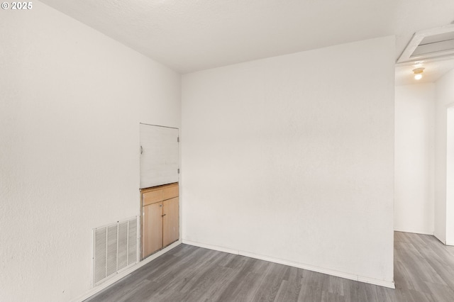 spare room featuring baseboards, wood finished floors, visible vents, and attic access