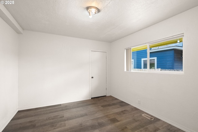 unfurnished room featuring a textured ceiling, wood finished floors, visible vents, and baseboards