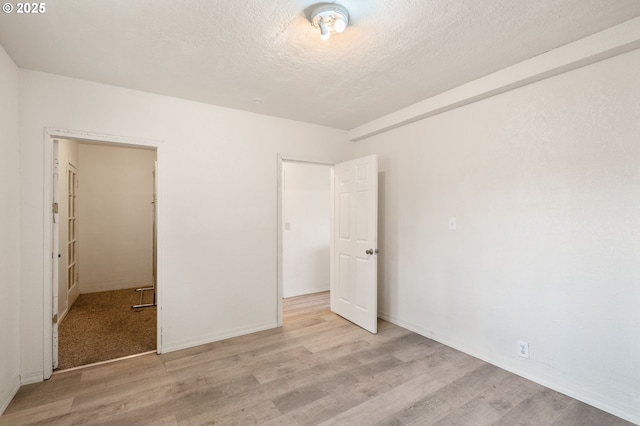 unfurnished bedroom with light wood-style floors, a textured ceiling, and baseboards