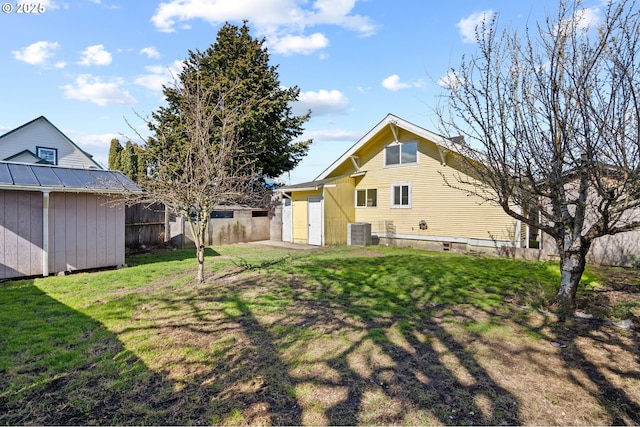 back of house with an outbuilding, a storage shed, central AC, fence, and a yard