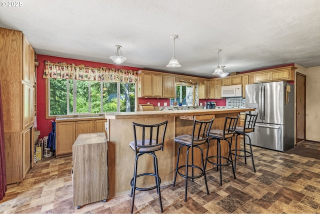 kitchen featuring hanging light fixtures, stainless steel refrigerator with ice dispenser, a wealth of natural light, and a breakfast bar area