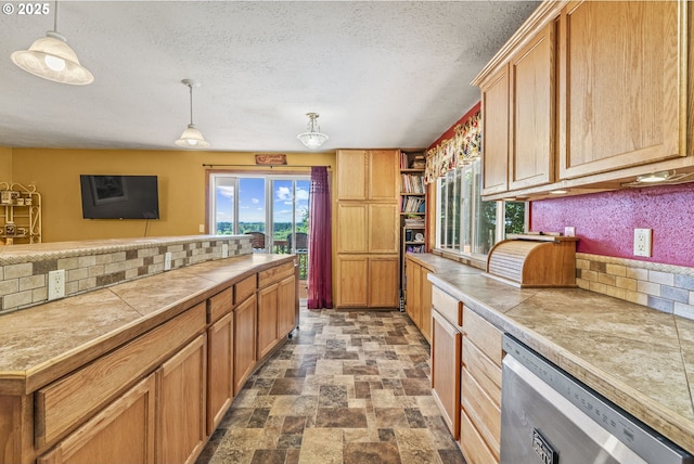 kitchen with hanging light fixtures, stainless steel dishwasher, and a textured ceiling