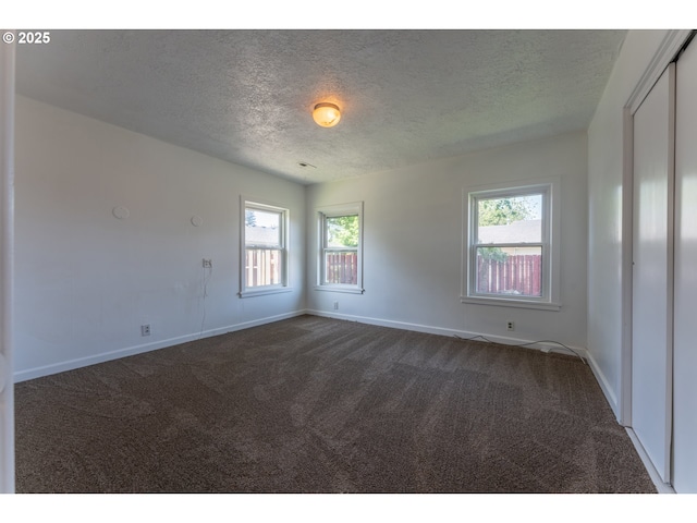 spare room with a textured ceiling, a healthy amount of sunlight, baseboards, and dark colored carpet