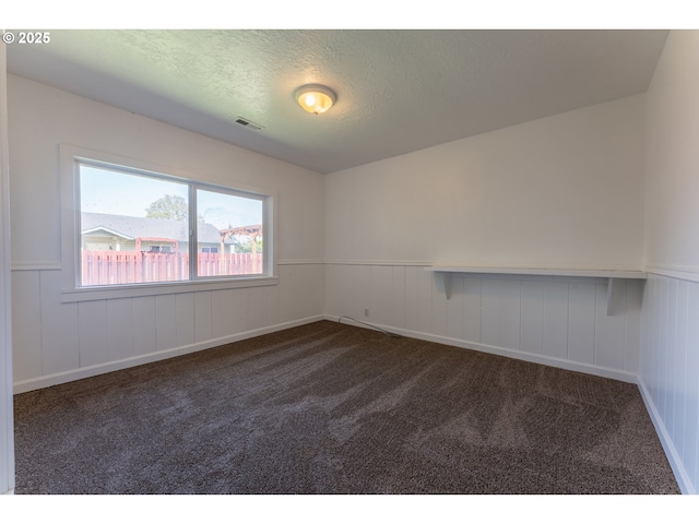 unfurnished room with a wainscoted wall, dark carpet, and visible vents