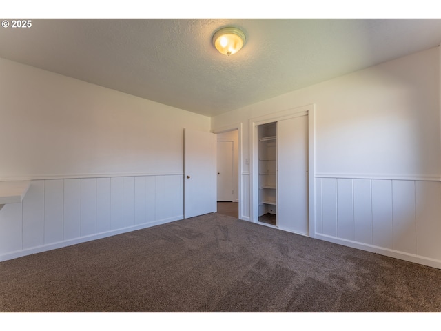 unfurnished bedroom featuring wainscoting, a closet, carpet flooring, and a textured ceiling