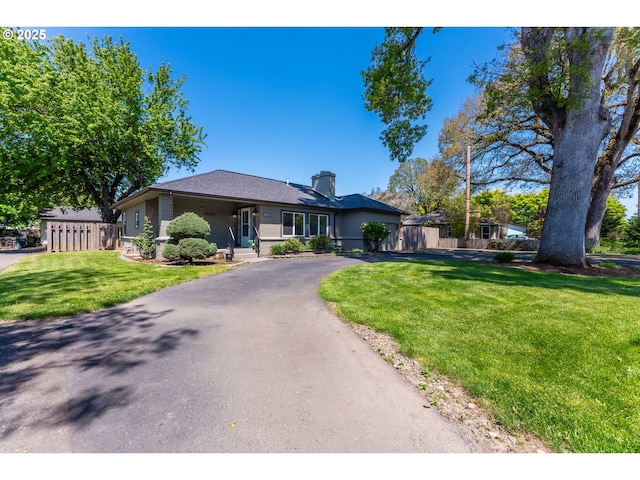 ranch-style house featuring a front lawn, fence, driveway, and a chimney