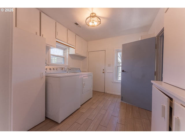 laundry room with cabinet space, separate washer and dryer, visible vents, and light wood-type flooring