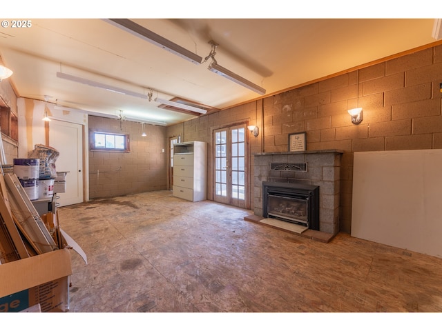 unfurnished living room featuring a fireplace with raised hearth, concrete block wall, and french doors