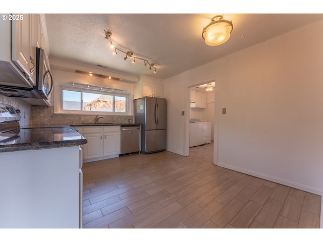 kitchen with a sink, stainless steel appliances, white cabinetry, tasteful backsplash, and washer and clothes dryer