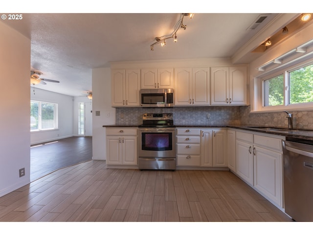 kitchen with appliances with stainless steel finishes, decorative backsplash, a sink, and light wood-style floors