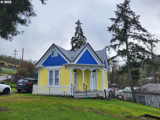 victorian-style house featuring a porch, fence, and a front lawn