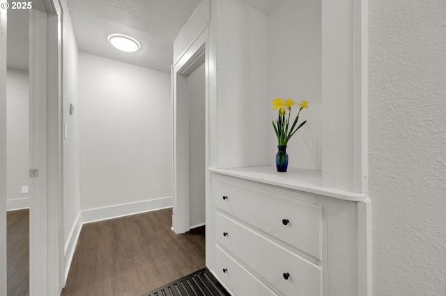 hall with dark wood finished floors, a textured ceiling, and baseboards