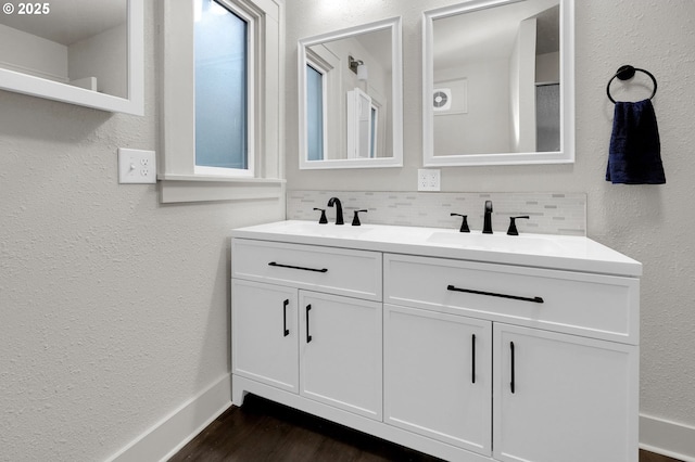 bathroom featuring a textured wall, wood finished floors, a sink, double vanity, and tasteful backsplash