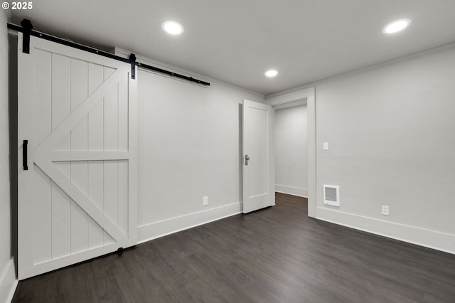 below grade area with visible vents, dark wood finished floors, baseboards, and a barn door