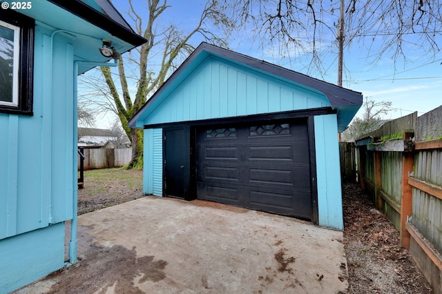 detached garage featuring concrete driveway and fence