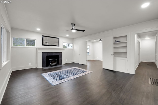 unfurnished living room with built in features, baseboards, visible vents, a ceiling fan, and dark wood-type flooring