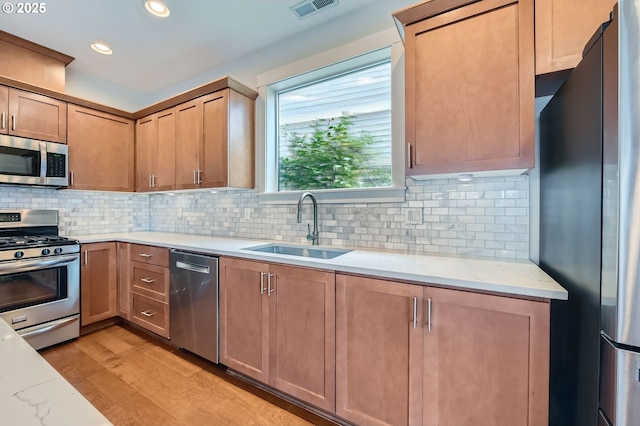kitchen featuring appliances with stainless steel finishes, a sink, light wood-style flooring, tasteful backsplash, and recessed lighting