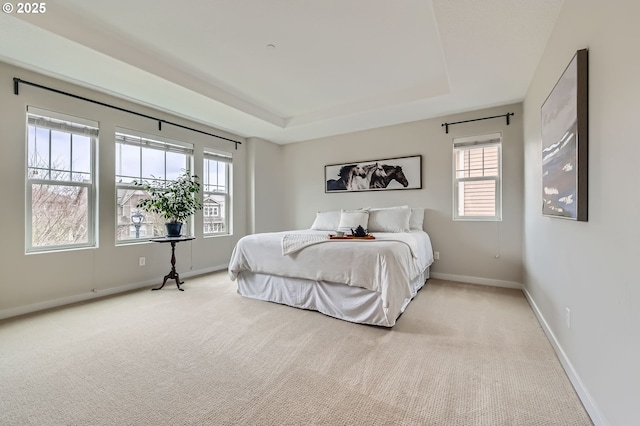bedroom featuring light carpet, a raised ceiling, multiple windows, and baseboards