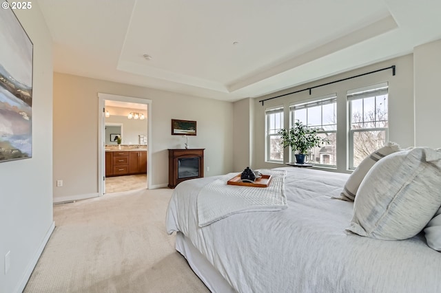 bedroom with a raised ceiling, light carpet, baseboards, connected bathroom, and a glass covered fireplace