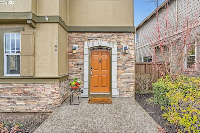 entrance to property featuring stone siding, fence, and stucco siding