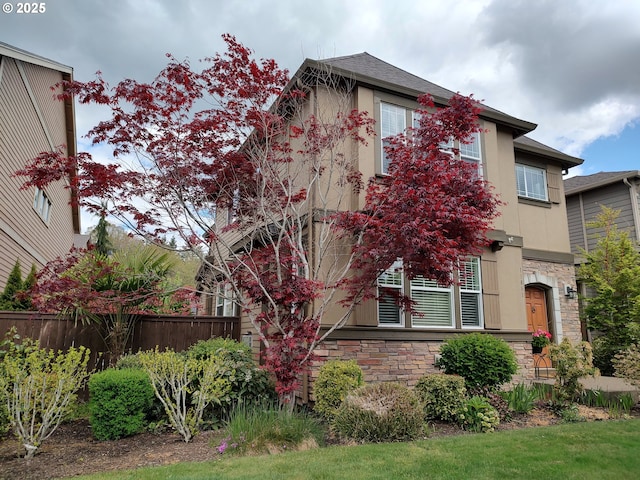 view of property hidden behind natural elements featuring stone siding, fence, and stucco siding