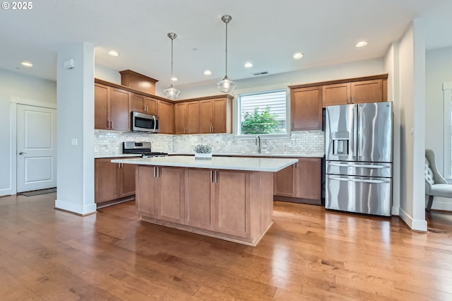 kitchen with stainless steel appliances, a center island, light countertops, light wood-type flooring, and a sink