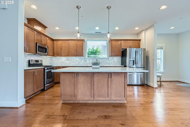 kitchen featuring appliances with stainless steel finishes, a kitchen island, baseboards, light countertops, and plenty of natural light