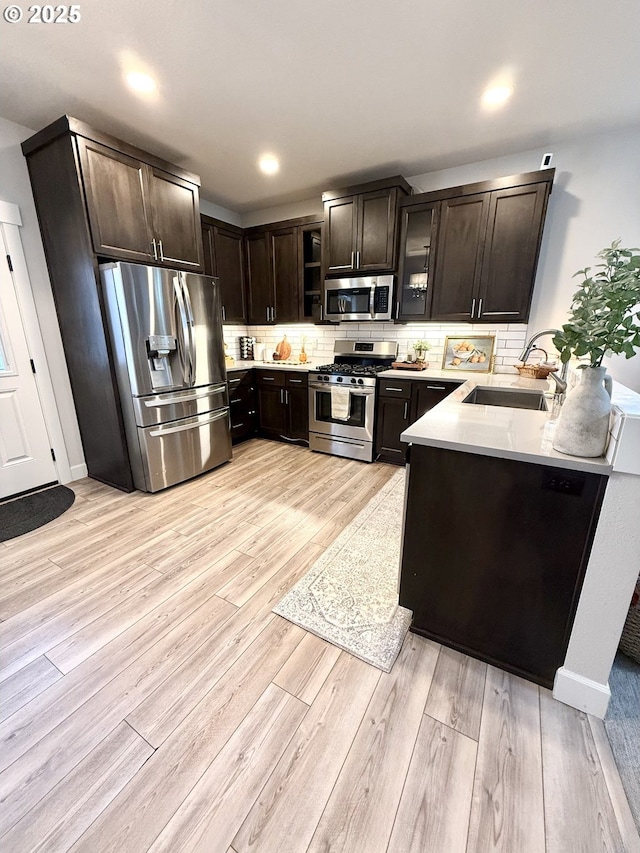 kitchen featuring sink, dark brown cabinets, light wood-type flooring, stainless steel appliances, and decorative backsplash