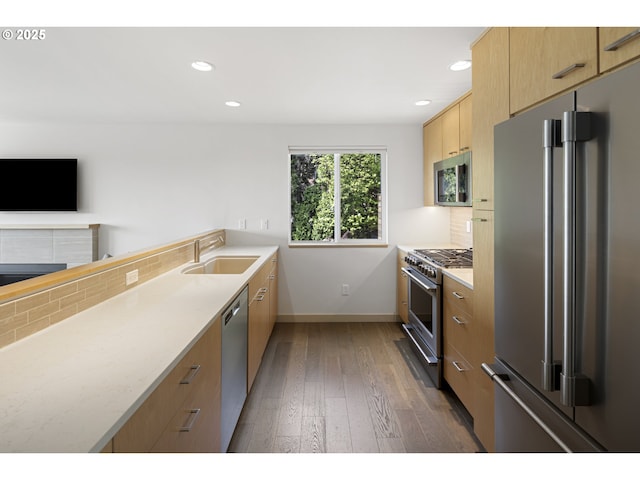 kitchen with decorative backsplash, dark wood-style flooring, high quality appliances, light brown cabinetry, and a sink
