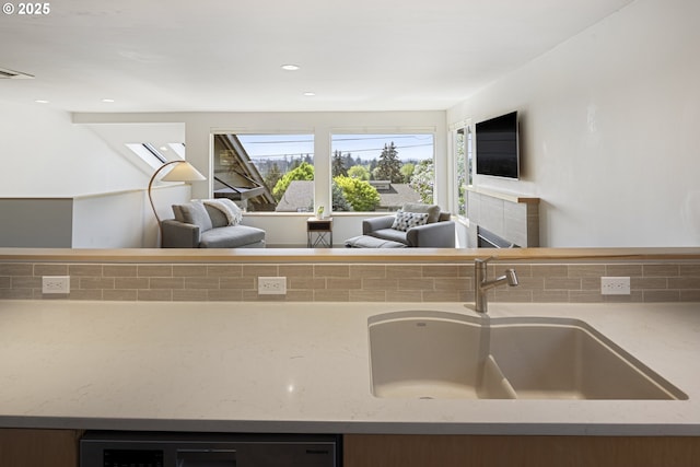 kitchen with a sink, light stone counters, decorative backsplash, and open floor plan