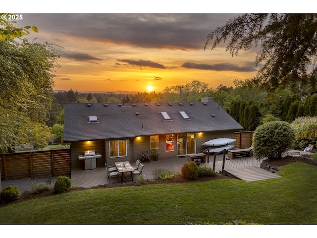 rear view of house featuring a yard, a deck, fence, and roof with shingles