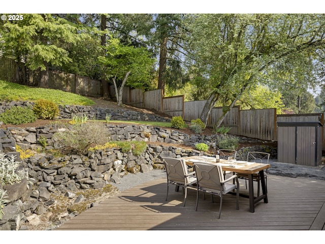 deck featuring a fenced backyard, a storage unit, outdoor dining space, and an outdoor structure