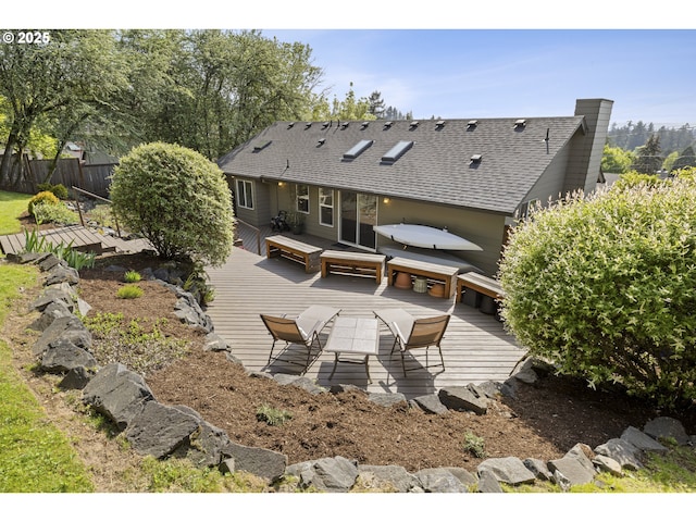 back of property featuring fence, a shingled roof, a wooden deck, outdoor dining area, and a chimney