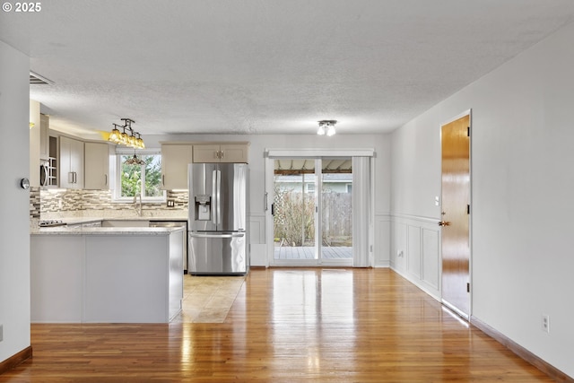 kitchen featuring a wainscoted wall, decorative backsplash, appliances with stainless steel finishes, light wood-style floors, and a textured ceiling