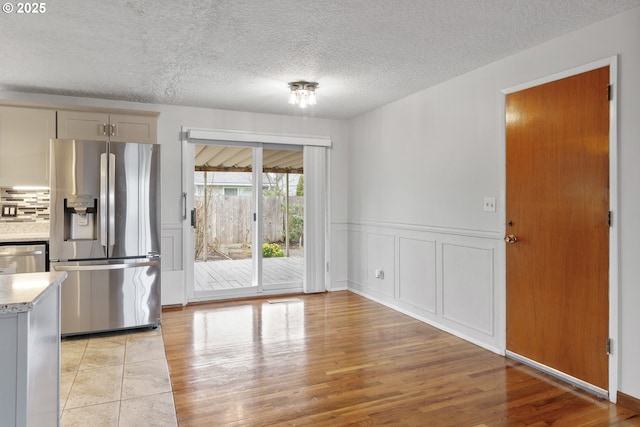 interior space featuring light wood finished floors, tasteful backsplash, a wainscoted wall, appliances with stainless steel finishes, and a textured ceiling