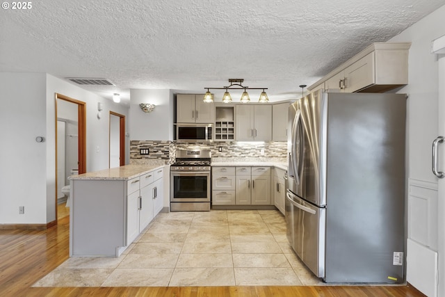 kitchen featuring visible vents, light stone countertops, decorative backsplash, appliances with stainless steel finishes, and a peninsula