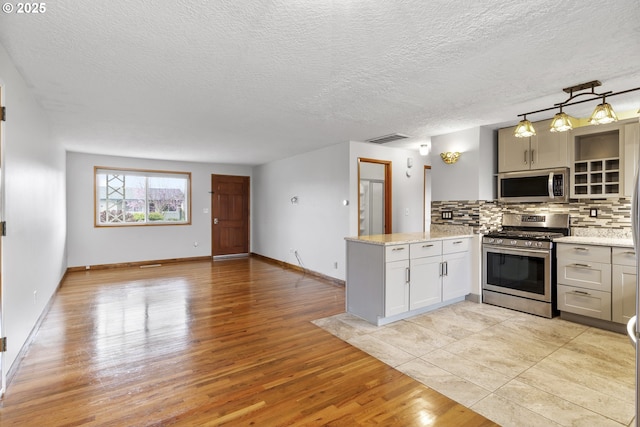 kitchen featuring visible vents, stainless steel appliances, a peninsula, light wood finished floors, and decorative backsplash