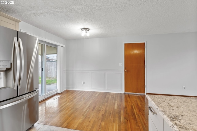 kitchen featuring a wainscoted wall, light wood finished floors, a textured ceiling, stainless steel fridge with ice dispenser, and a decorative wall