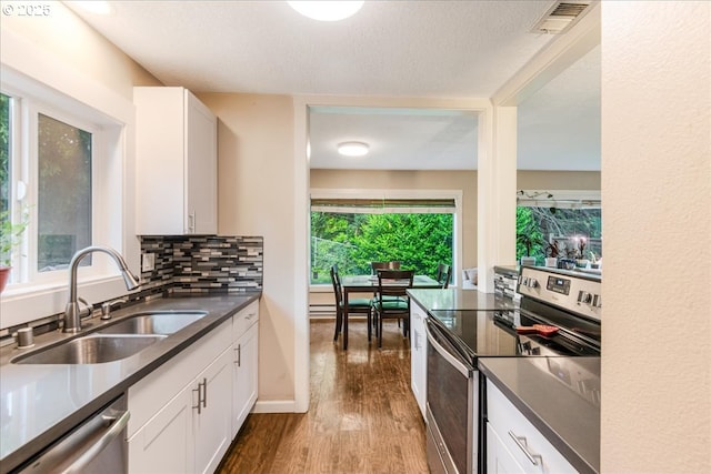 6926 SE Deardorff Rd, Portland, OR 97236 - kitchen with stainless steel appliances, a sink, wood finished floors, dark countertops, and white cabinetry