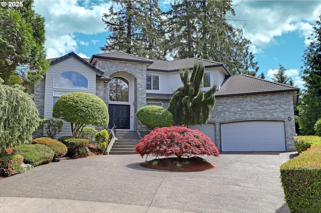 mediterranean / spanish home featuring a tile roof, driveway, an attached garage, and brick siding