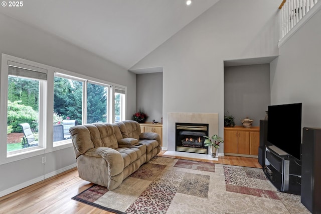 living room featuring high vaulted ceiling, light wood-style floors, a fireplace with flush hearth, and baseboards