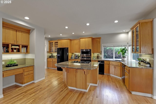 kitchen with black fridge, stainless steel microwave, decorative backsplash, a kitchen island, and light wood finished floors