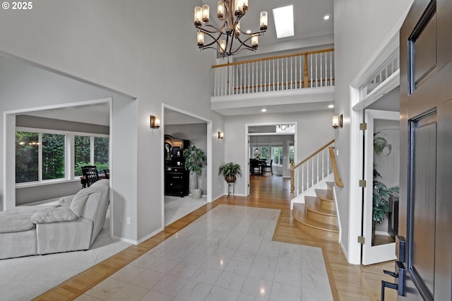 foyer entrance featuring stairs, a high ceiling, a chandelier, baseboards, and light wood-style flooring