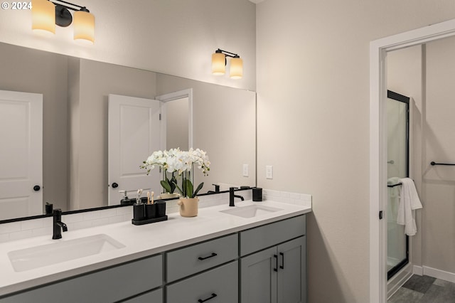 bathroom featuring baseboards, a stall shower, double vanity, and a sink