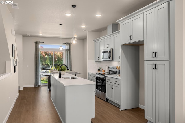 kitchen featuring dark wood-type flooring, stainless steel appliances, an island with sink, and a sink