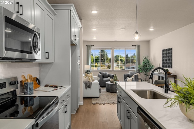 kitchen featuring pendant lighting, sink, backsplash, stainless steel appliances, and light wood-type flooring