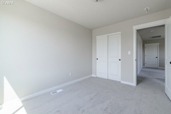 unfurnished bedroom with light colored carpet and a closet